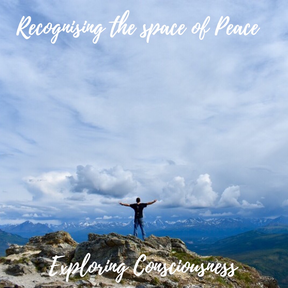 Man on mountain top, arms outstretched, peaceful view.