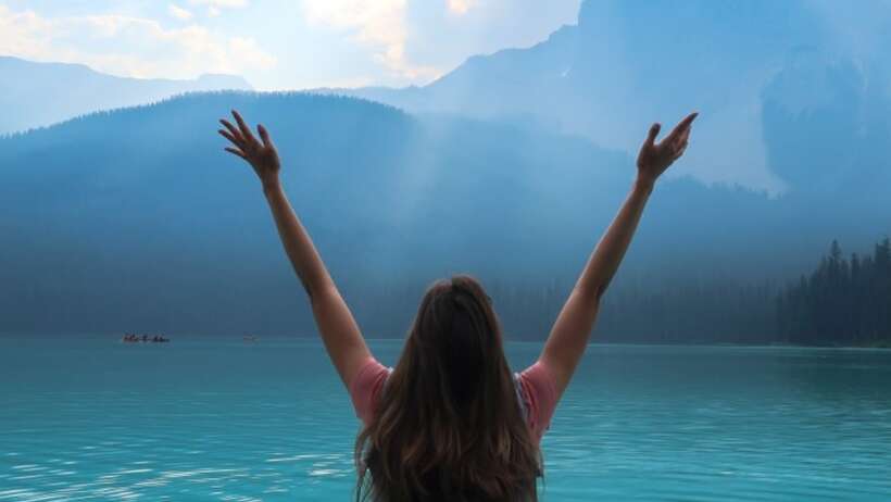Woman canoeing on lake, arms raised in gratitude.