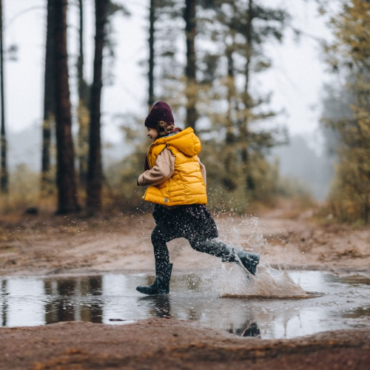 Girl in puddle in woods, yellow jacket.