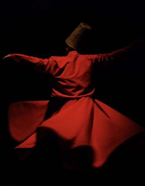 Whirling Dervish in red robe, black background.